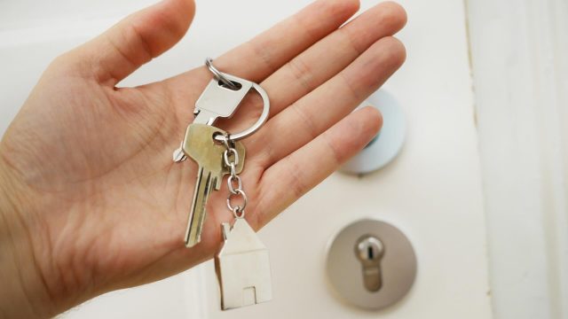 Eine Person, die einen Hausschlüssel in der Hand hält, der den Besitz oder den Zugang zu einem Haus symbolisiert.